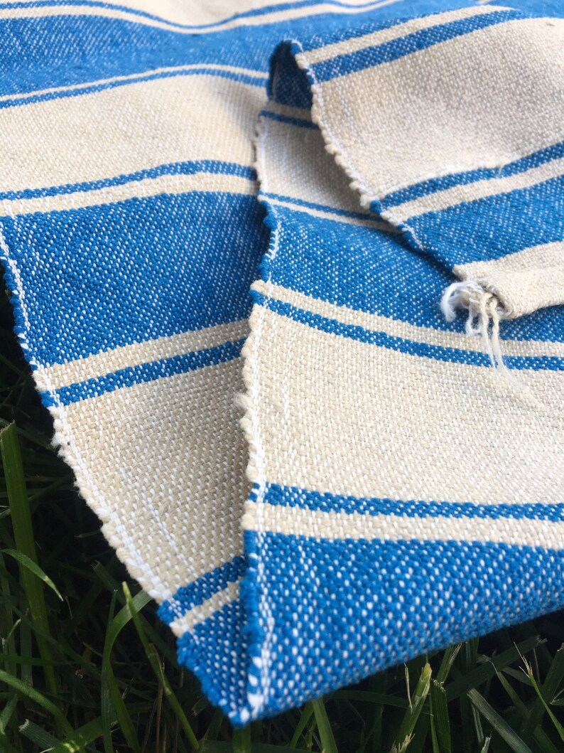 Puede incluir: Una tela de rayas azules y blancas con una textura rugosa. La tela est&aacute; doblada por la mitad y los bordes est&aacute;n deshilachados.