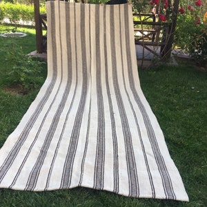 May include: A white and black striped rug with a woven texture. The rug is laid out on a grassy lawn.