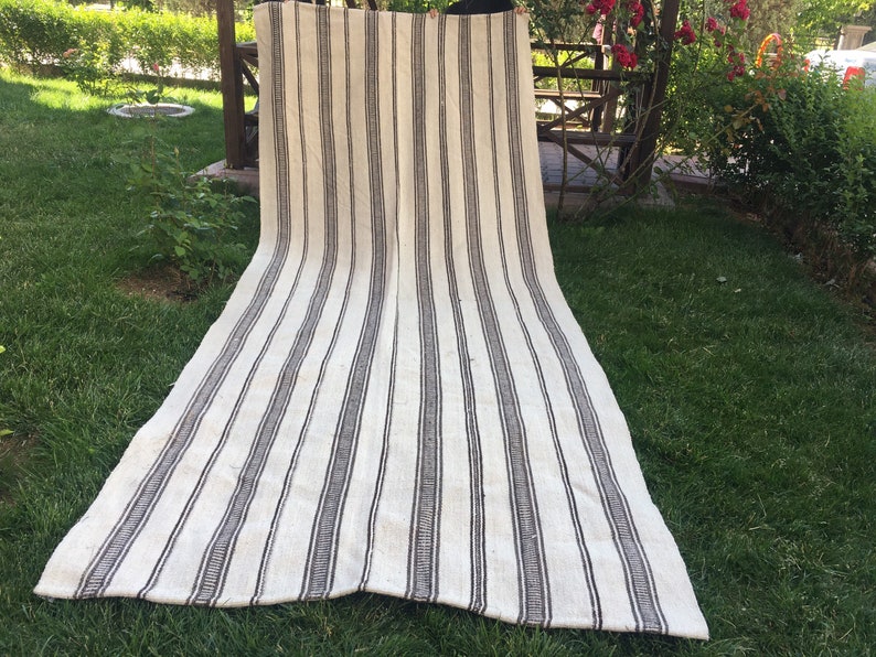 May include: A white and black striped rug with a woven texture. The rug is laid out on a grassy lawn.