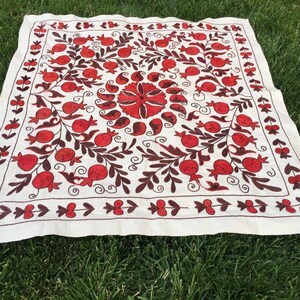 May include: White fabric square with red and brown embroidery of pomegranates and floral designs.