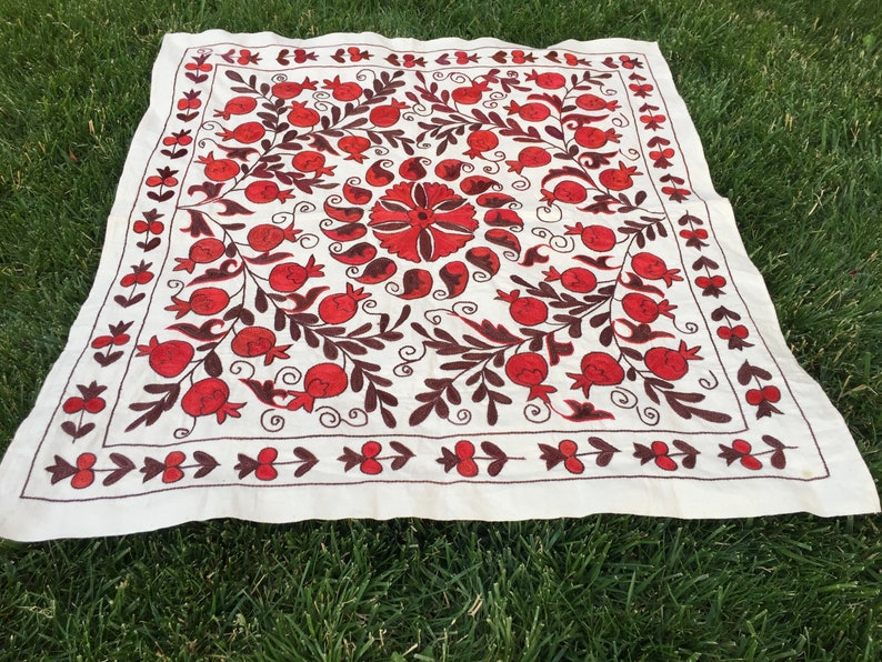 May include: White fabric square with red and brown embroidery of pomegranates and floral designs.