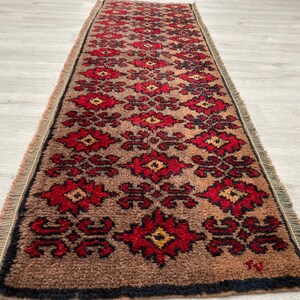 Pode incluir: Um tapete corredor retangular com fundo castanho e um padrão floral repetido em vermelho e preto. O tapete tem uma borda preta e bordas com franjas. O tapete tem aproximadamente 60 cm de largura e 180 cm de comprimento.