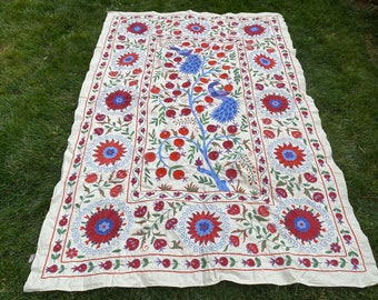 Puede incluir: Una tela de algodón blanca con un diseño de bordado hecho a mano que presenta un árbol azul y verde con granadas rojas y dos pavos reales. El borde está decorado con motivos florales rojos y azules.