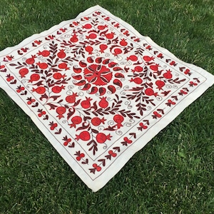 May include: White square fabric with red and brown embroidery of pomegranates and floral designs.