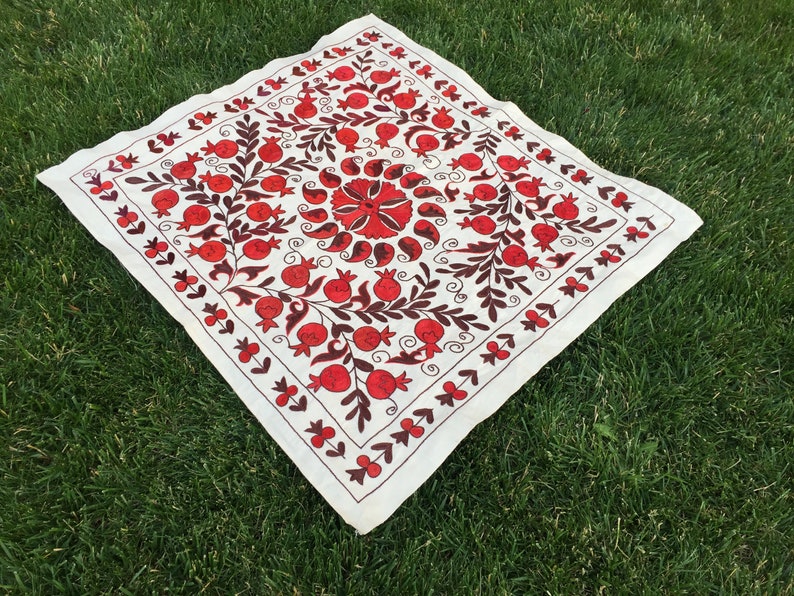 May include: White square fabric with red and brown embroidery of pomegranates and floral designs.
