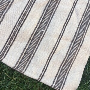May include: A white and brown striped rug with a woven texture. The rug is made of natural fibres and has a rustic look.