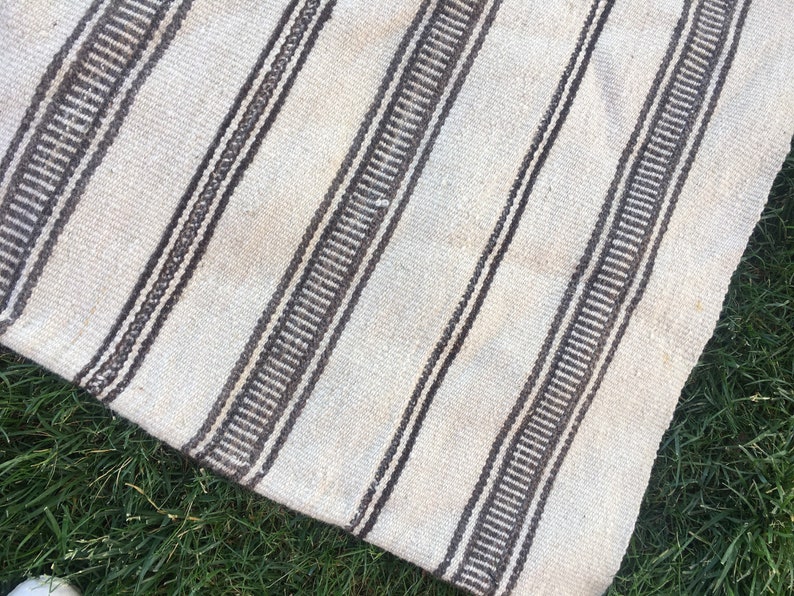 May include: A white and brown striped rug with a woven texture. The rug is made of natural fibres and has a rustic look.