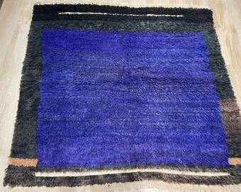 Puede incluir: Una alfombra azul y negra con textura peluda. La alfombra tiene un borde negro y marrón.