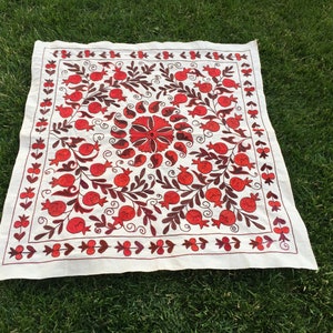May include: White fabric square with red and brown embroidery of pomegranates and floral designs.