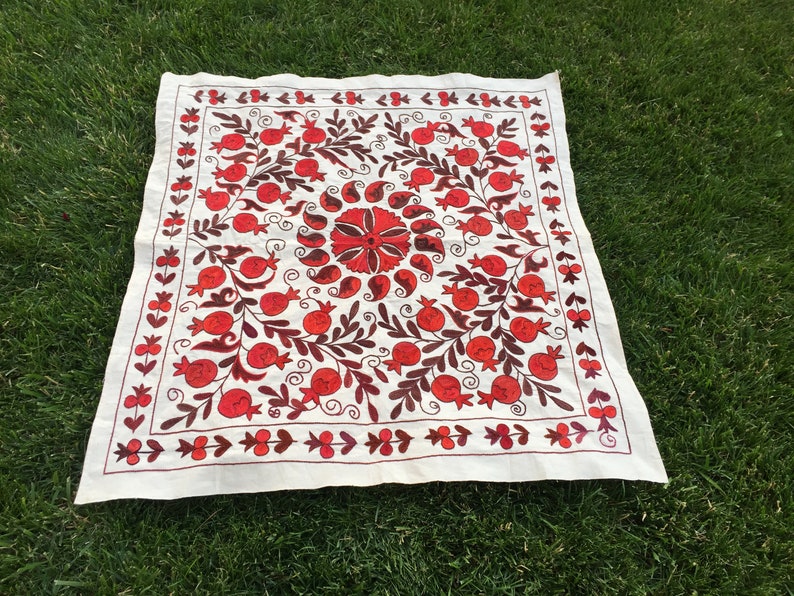 May include: White fabric square with red and brown embroidery of pomegranates and floral designs.
