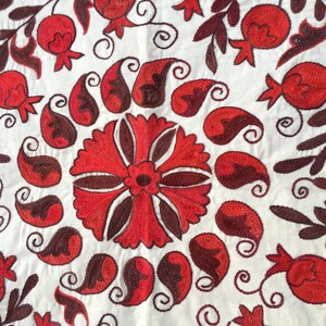 May include: White fabric with red and brown embroidery. The design features a large central flower surrounded by paisley shapes and smaller flowers.