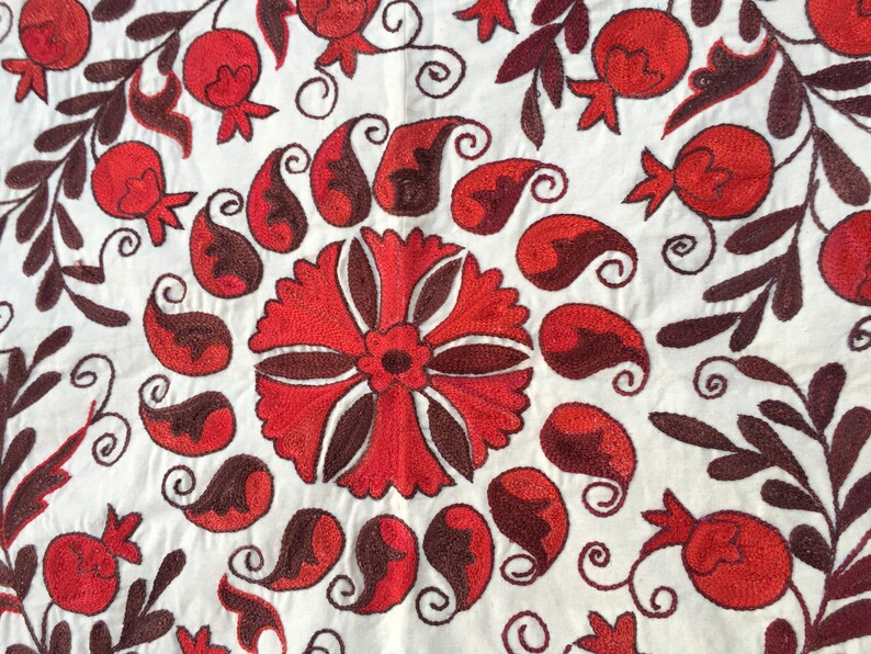 May include: White fabric with red and brown embroidery. The design features a large central flower surrounded by paisley shapes and smaller flowers.