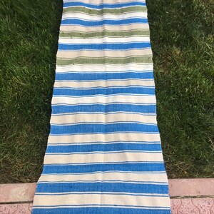 Puede incluir: Una alfombra larga y rayada con rayas azules y blancas alternadas. La alfombra tiene algunas rayas verdes en la parte superior.