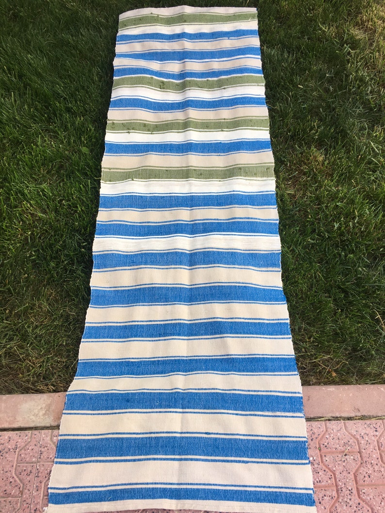 Puede incluir: Una alfombra larga y rayada con rayas azules y blancas alternadas. La alfombra tiene algunas rayas verdes en la parte superior.