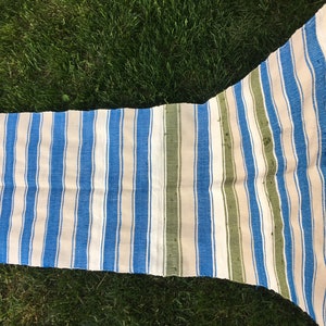 Puede incluir: Una alfombra de tejido a rayas con rayas azules, blancas y verdes. La alfombra est&aacute; tejida y tiene un aspecto ligeramente desgastado.
