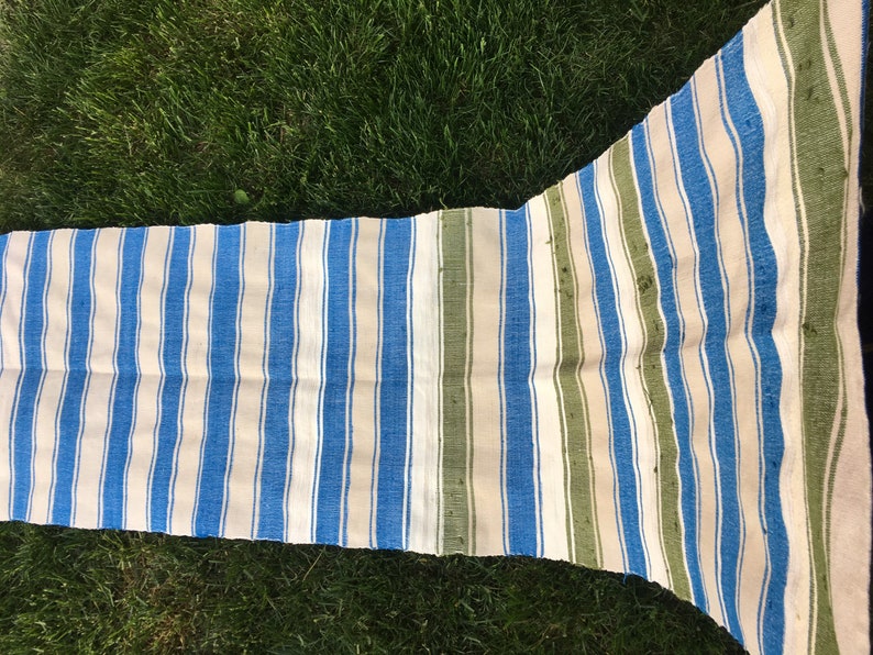 Puede incluir: Una alfombra de tejido a rayas con rayas azules, blancas y verdes. La alfombra est&aacute; tejida y tiene un aspecto ligeramente desgastado.