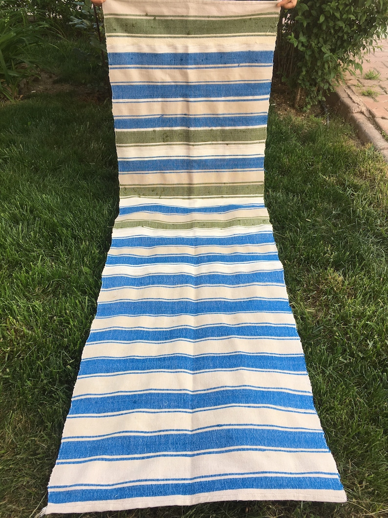 Puede incluir: Una alfombra larga y rayada con rayas azules y blancas alternadas. La alfombra tiene una secci&oacute;n rayada verde y blanca en la parte superior.