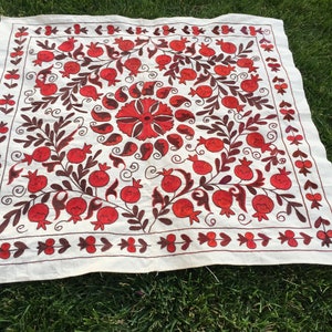 May include: A white linen tablecloth with a red and brown embroidered design of pomegranates and leaves.