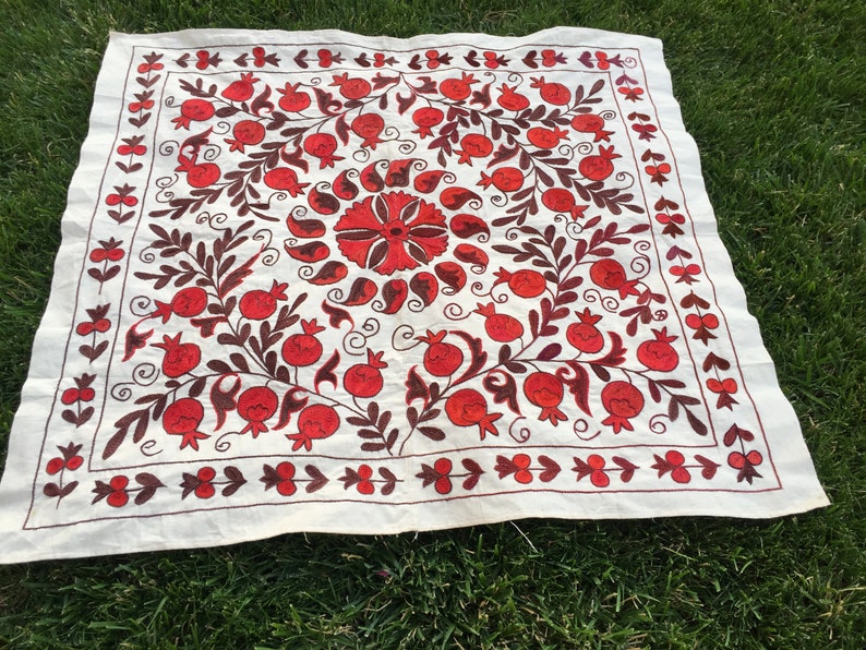 May include: A white linen tablecloth with a red and brown embroidered design of pomegranates and leaves.