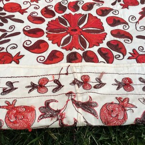May include: A white fabric tablecloth with red and brown embroidery of floral and paisley designs. The tablecloth has a border of smaller floral designs.