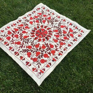 May include: White fabric square with red and brown embroidery of pomegranates and floral designs.