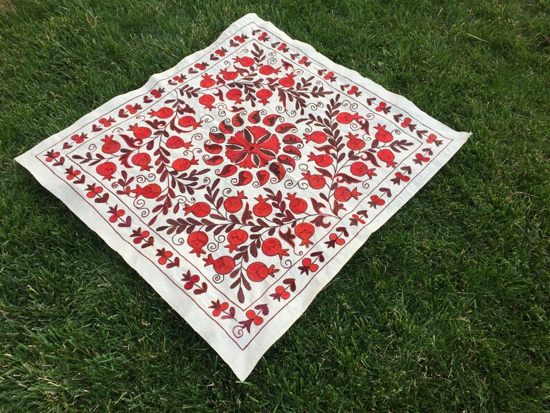 May include: White fabric square with red and brown embroidery of pomegranates and floral designs.