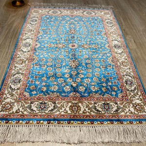 May include: A blue and cream patterned rug with a floral design and fringe on the edges.