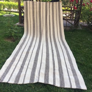 May include: A white and black striped rug with a woven texture. The rug is laid out on a grassy lawn.