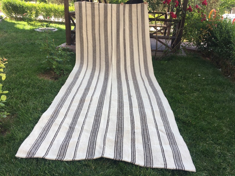 May include: A white and black striped rug with a woven texture. The rug is laid out on a grassy lawn.