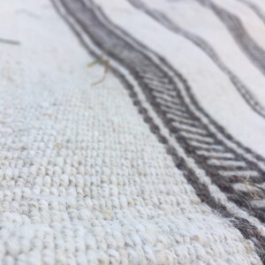 May include: Close-up of a white and grey woven rug with a textured surface. The rug has a striped pattern with alternating white and grey stripes.