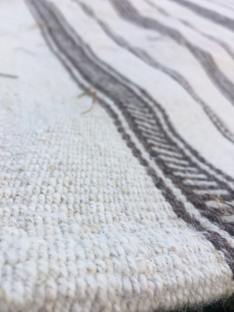 May include: Close-up of a white and grey woven rug with a textured surface. The rug has a striped pattern with alternating white and grey stripes.