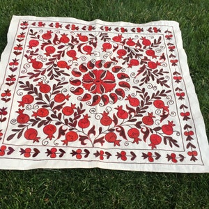 May include: A white linen square embroidered with a red and brown floral design. The design features pomegranates, leaves, and swirls.