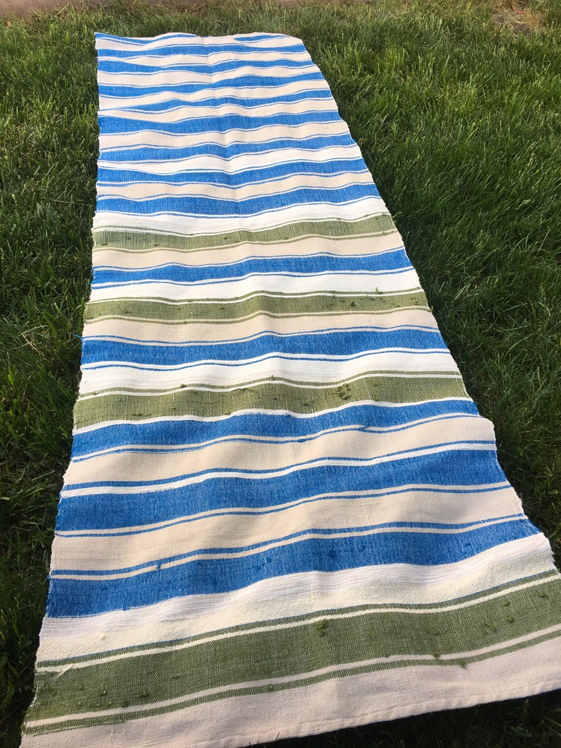 Puede incluir: Una alfombra larga y rayada con rayas azules, blancas y verdes. La alfombra est&aacute; hecha de un tejido tejido y tiene una superficie ligeramente texturizada.
