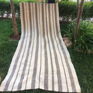 May include: A long, white and brown striped rug with a woven texture. The rug is laid out on a grassy lawn.