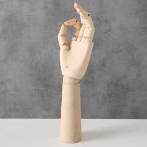 Könnte beinhalten: Hölzernes Handmodell mit beweglichen Fingern, in der 'Okay'-Geste dargestellt. Die Hand ist aus Naturholz gefertigt und hat eine glatte Oberfläche. Die Hand ist an einer Holzbasis befestigt.