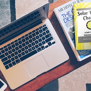 May include: A yellow and gray self-guided release journal with the title "Solar Plexus Chakra" and the website "www.rasathi.com". The journal is on top of a magazine with the title "The Design" and the word "Architecture" on the cover.