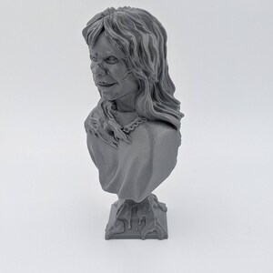 May include: A gray 3D printed bust of a woman with long hair. The bust is on a base that looks like it is made of stone.