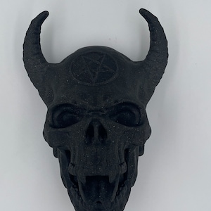 May include: A black skull with horns and a pentagram on the forehead. The skull is detailed with teeth and eye sockets.