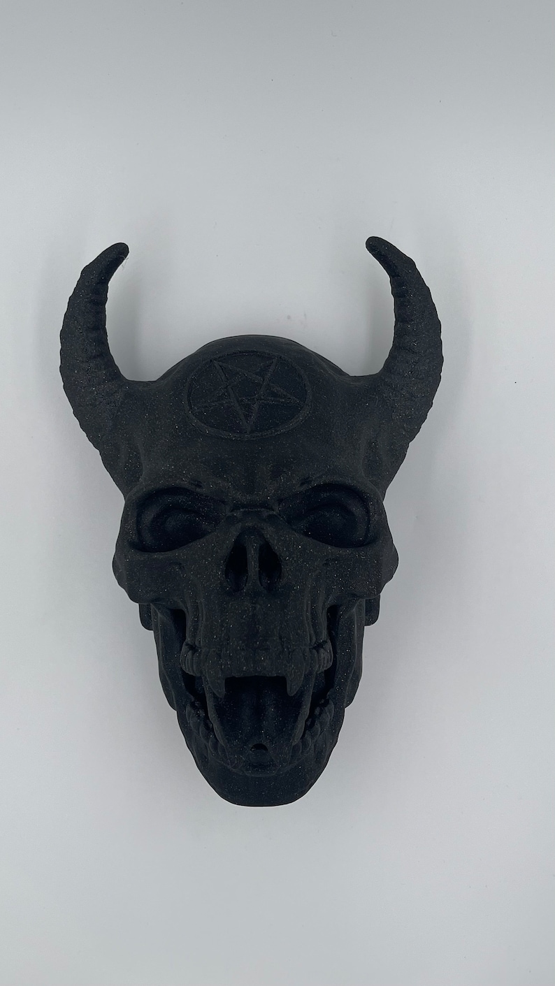 May include: A black skull with horns and a pentagram on the forehead. The skull is detailed with teeth and eye sockets.
