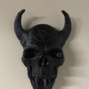 May include: A black skull with horns and a pentagram on the forehead. The skull is made of plastic and has a detailed design.