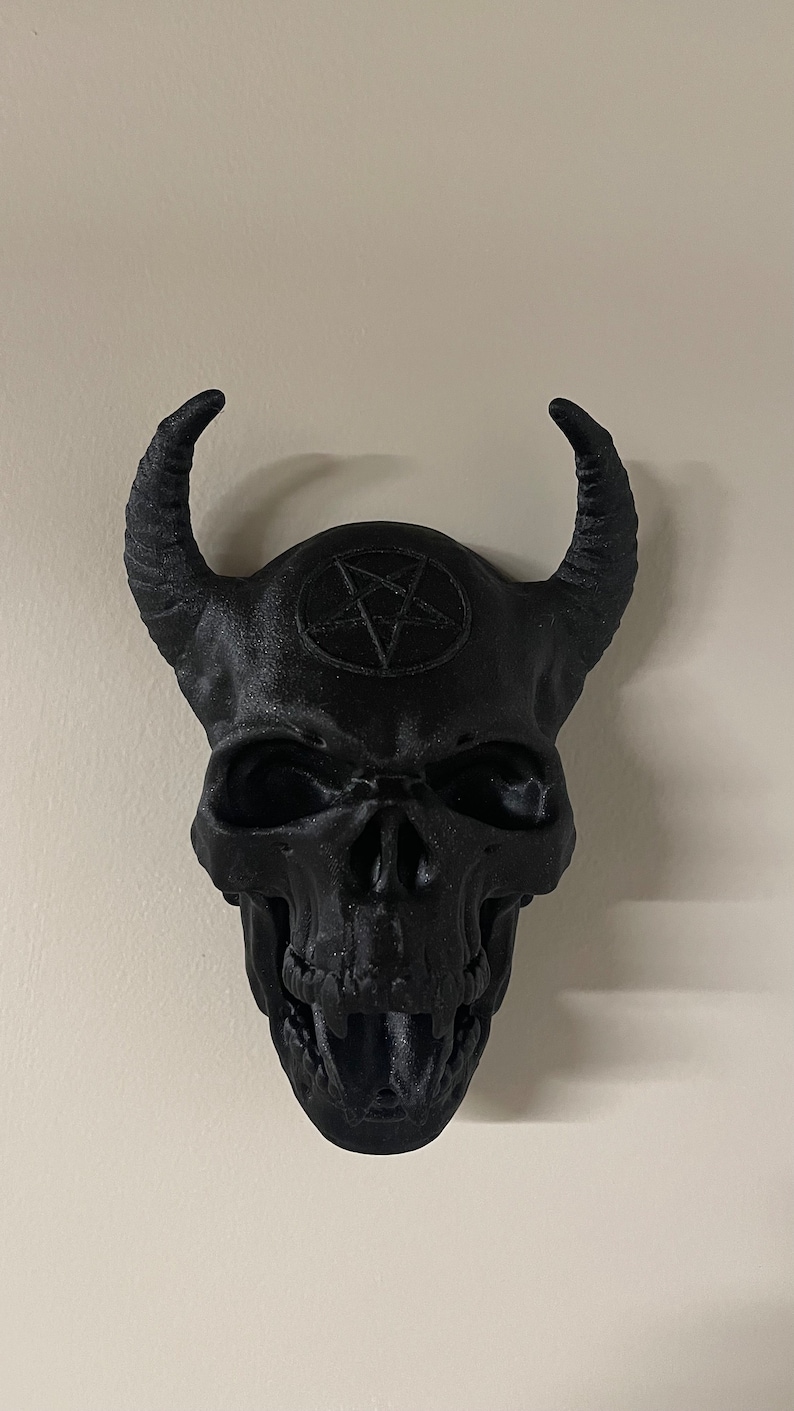 May include: A black skull with horns and a pentagram on the forehead. The skull is made of plastic and has a detailed design.