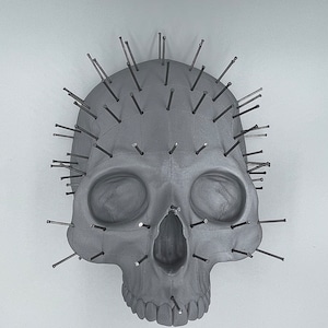 May include: A gray skull sculpture with numerous black metal pins protruding from the top of the skull.