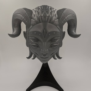 May include: A gray 3D printed sculpture of a face with horns and multiple eyes. The sculpture is on a black stand.