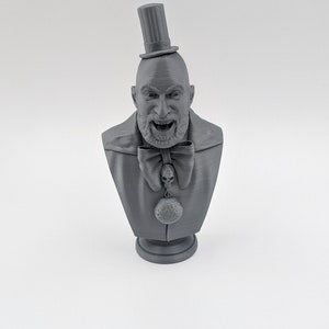 May include: A gray 3D printed bust of a man wearing a top hat, bow tie, and a skull pendant. The man has a beard and mustache and is smiling.