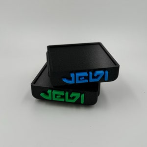 May include: Two black square coasters with the word "JEVI" printed on them in blue and green.