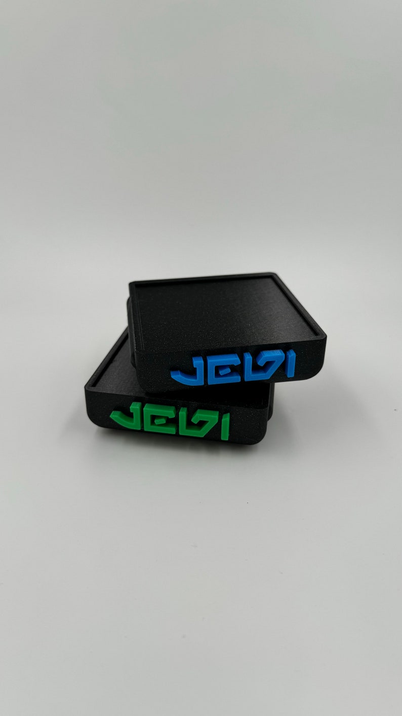 May include: Two black square coasters with the word "JEVI" printed on them in blue and green.