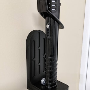 May include: Black lightsaber and wall mount. The lightsaber has a black handle with silver accents and a clear blade. The wall mount is also black and designed to hold the lightsaber securely.