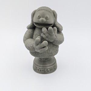 May include: A gray 3D printed bust of a furry character with a large smile and outstretched arms. The bust is on a base with the word "Muppets" inscribed on it.