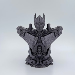 May include: A 3D printed model of a robot, featuring a detailed design with a metallic gray finish. The robot has a humanoid torso with a large head and wings.