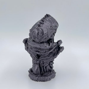 May include: A 3D printed figurine of a creature with a large head and a body that resembles a twisted, gnarled tree. The creature is painted in a dark gray color.